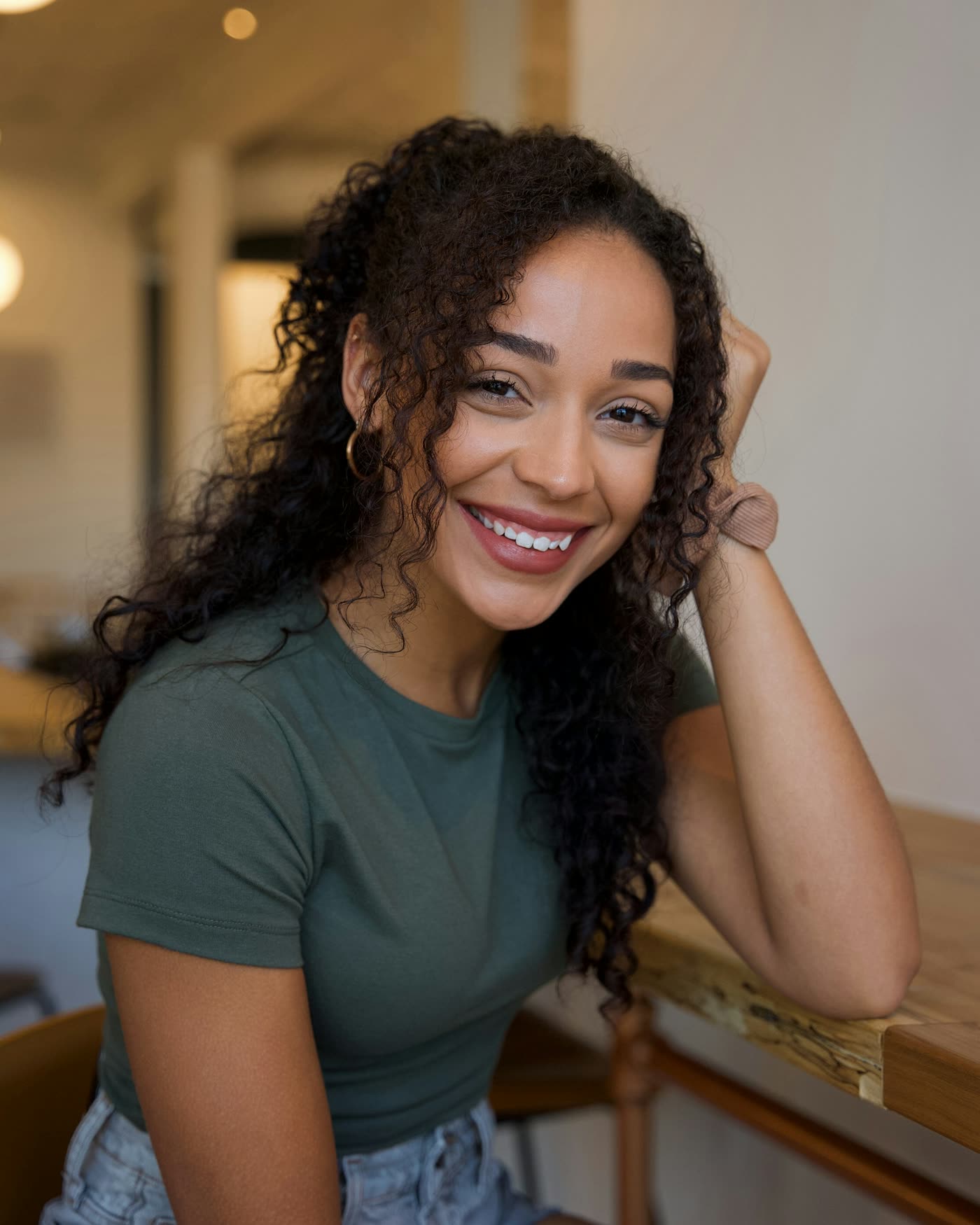 Marina Lobo, nutricionista, sorrindo, de camiseta verde, apoiada em uma mesa de madeira